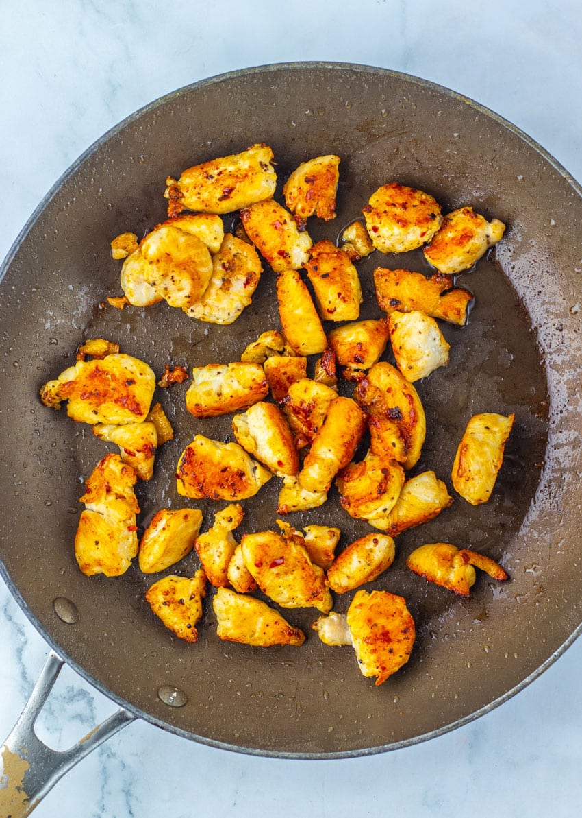 GOLDEN BROWN SAUTEED CHICKEN CHUNKS IN A LARGE FRYING PAN