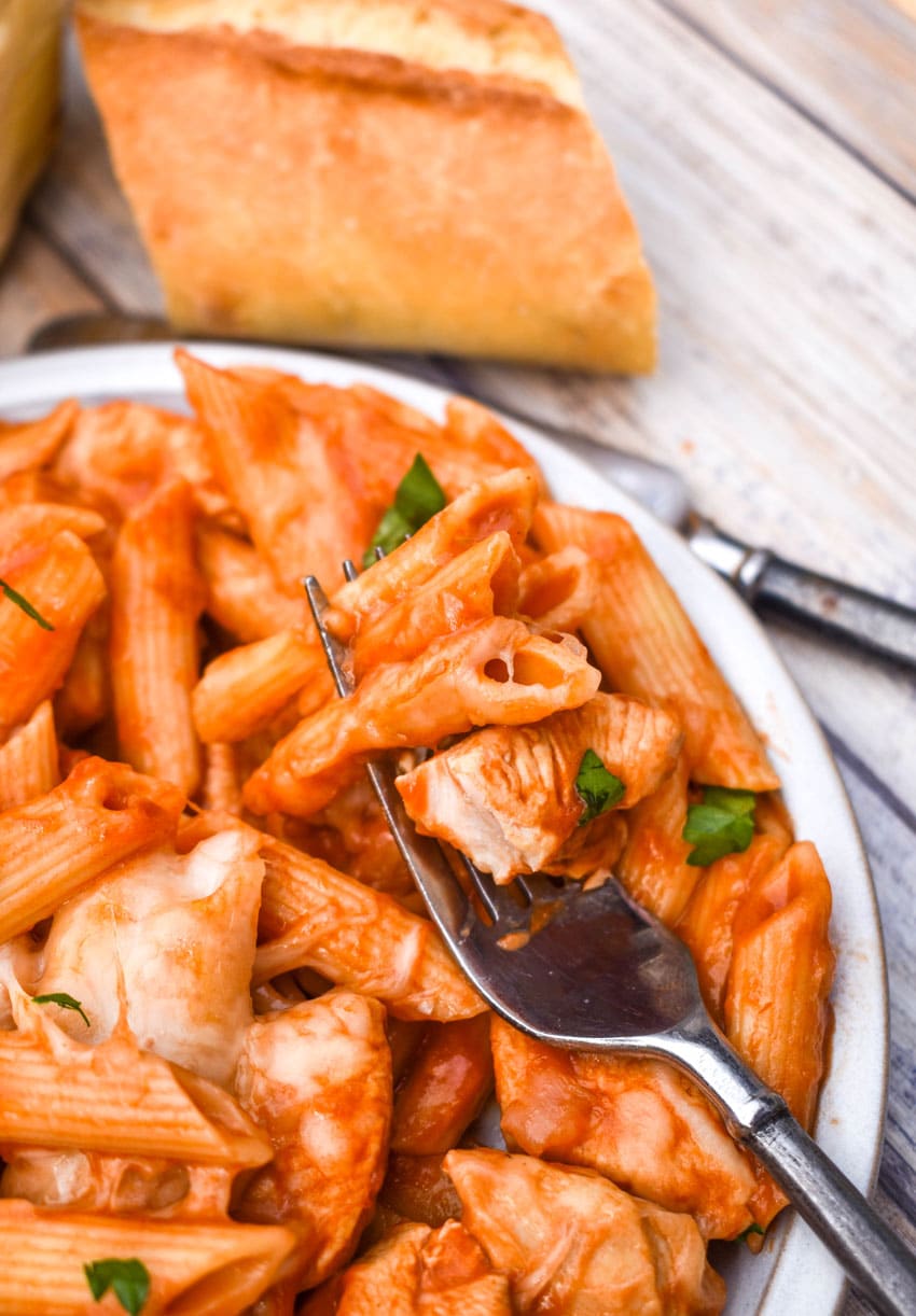 a silver fork scooping instant pot chicken parmesan pasta off of a white plate