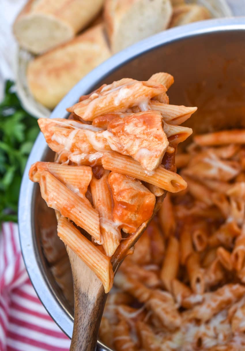 a wooden spoon holding up a scoop of chicken parmesan pasta