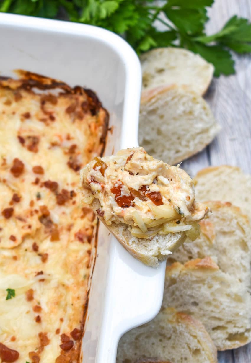 a marry me chicken dip topped slice of baguette bread resting on the edge of a white baking dish