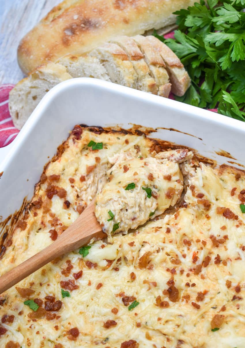 a wooden spoon scooping marry me chicken dip out of a white baking dish