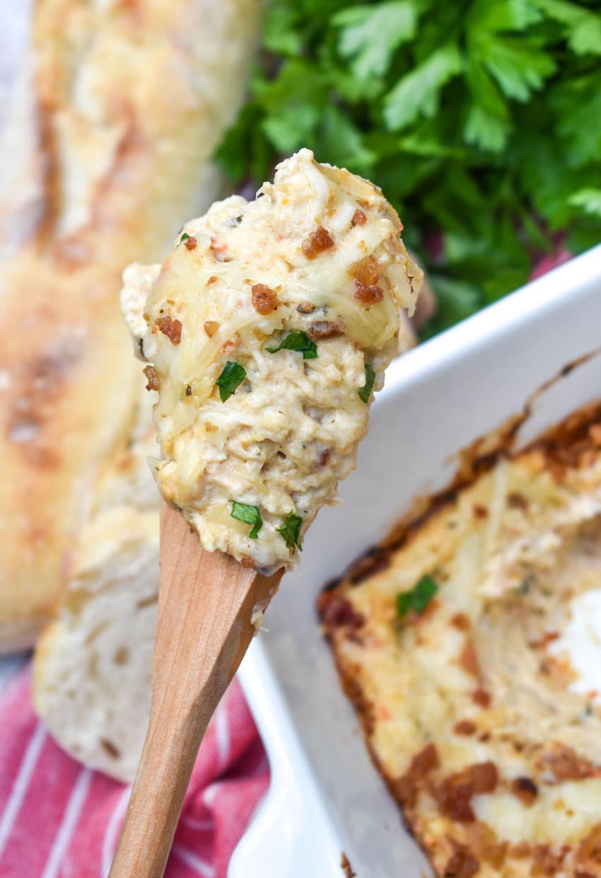 a wooden spoon holding up a scoop of marry me chicken dip