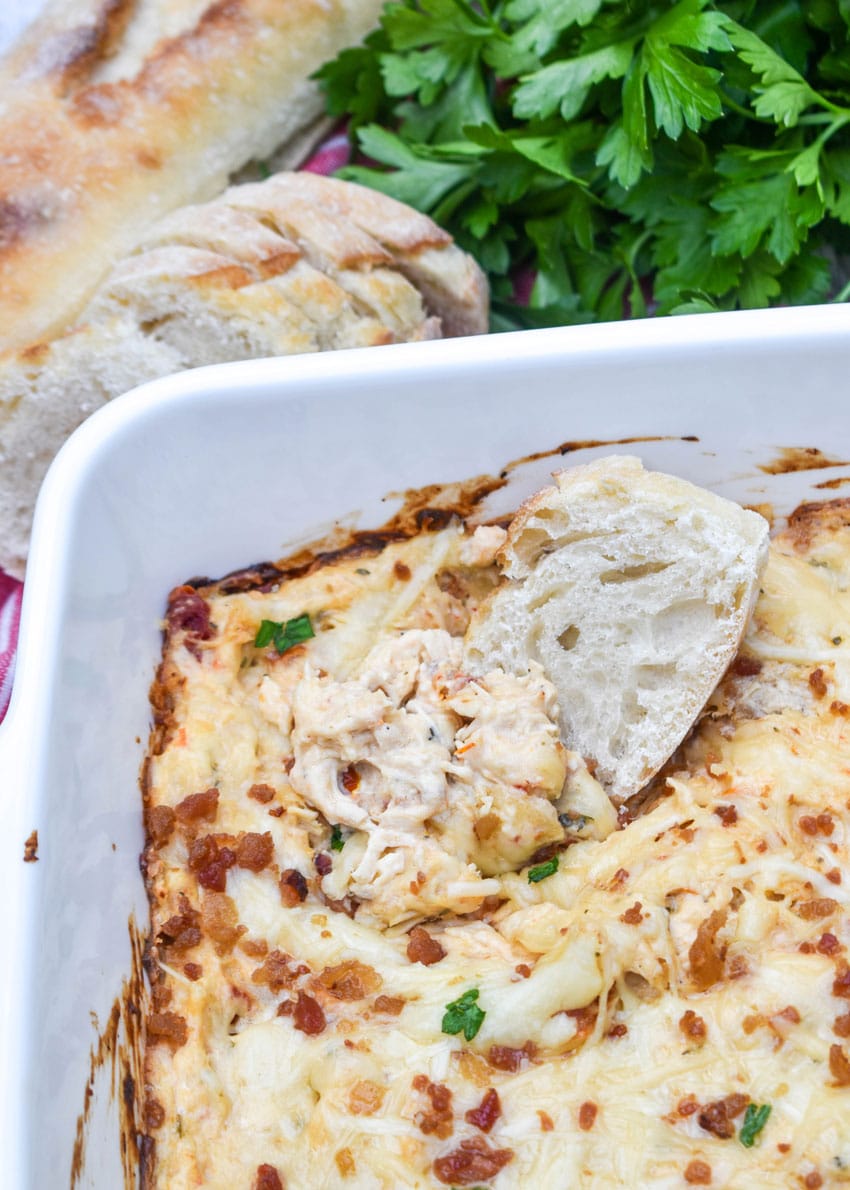 a baguette slice dipping into marry me chicken dip in a white baking dish