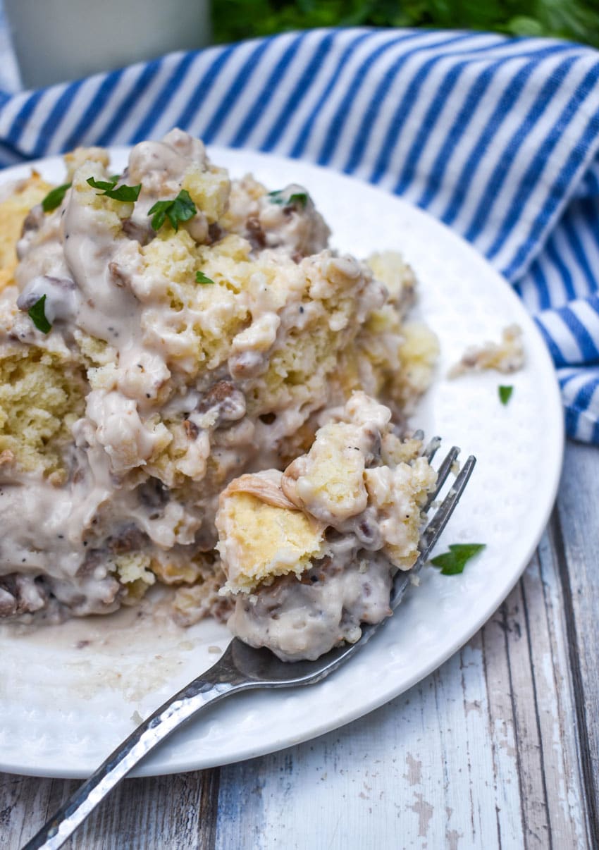 a silver fork scooping sausage gravy and biscuits off a white plate