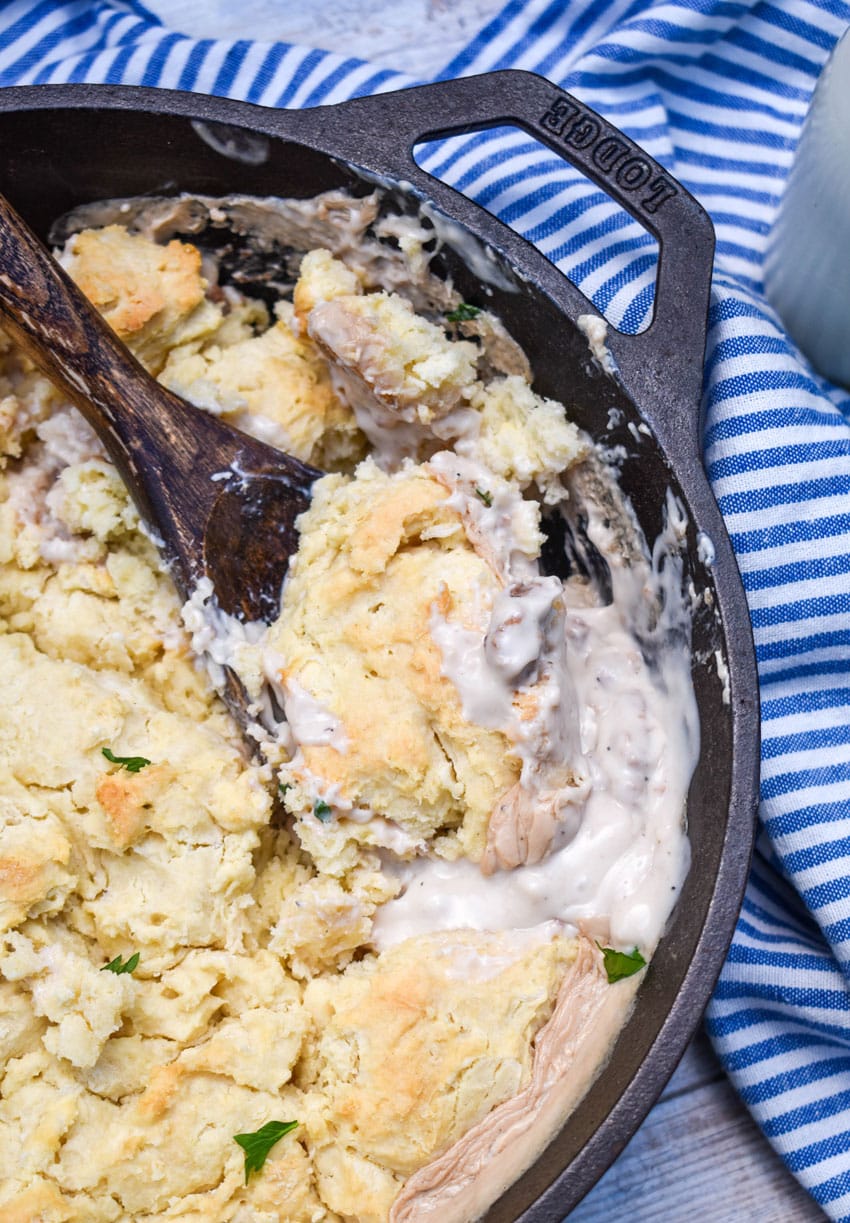 a wooden spoon scooping sausage gravy and biscuits out of a cast iron skillets