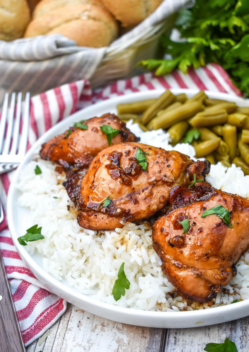 three balsamic chicken thighs over steamed white rice on a white plate