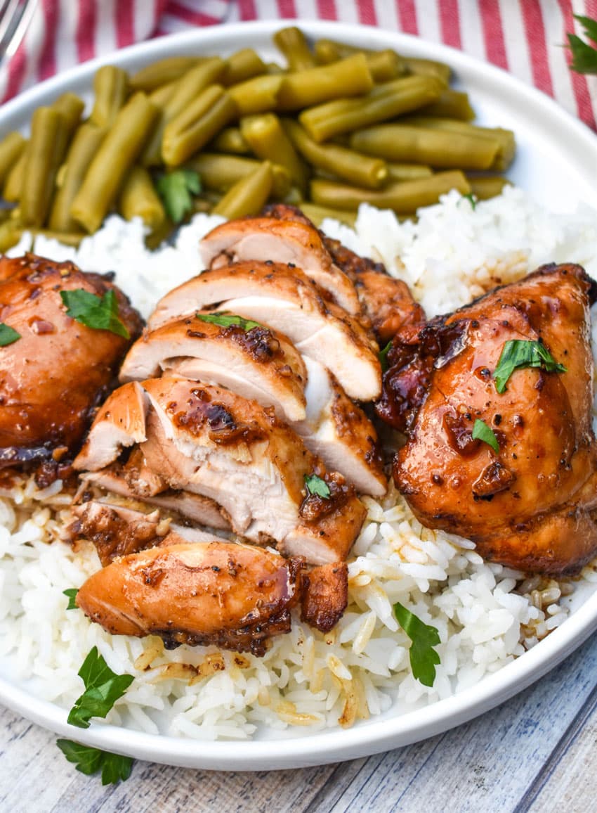 three balsamic chicken thighs over steamed white rice on a white plate