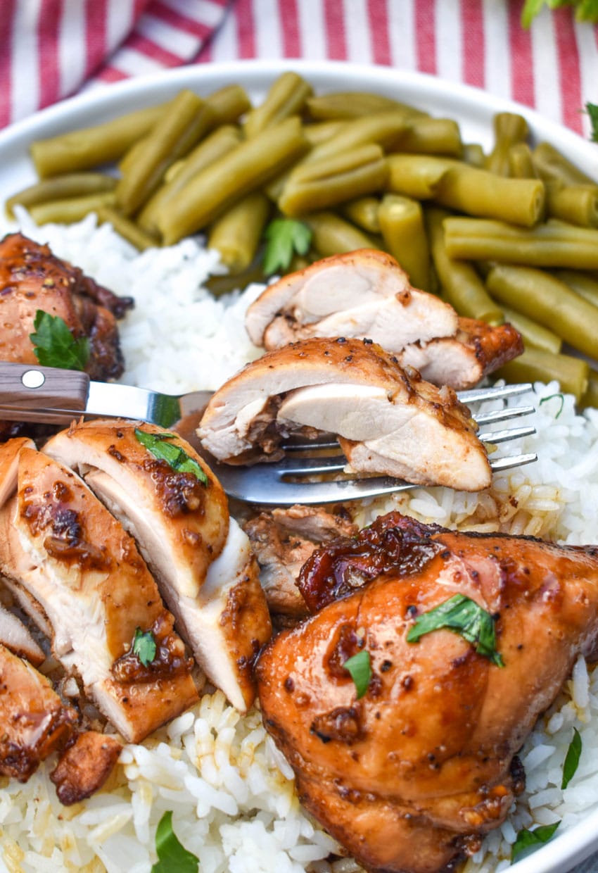 three balsamic chicken thighs over steamed white rice on a white plate