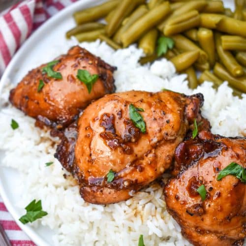 three balsamic chicken thighs over steamed white rice on a white plate