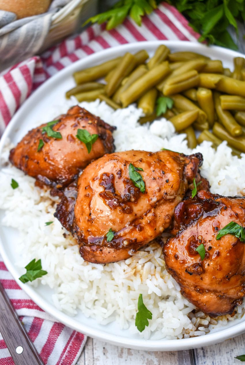 three balsamic chicken thighs over steamed white rice on a white plate