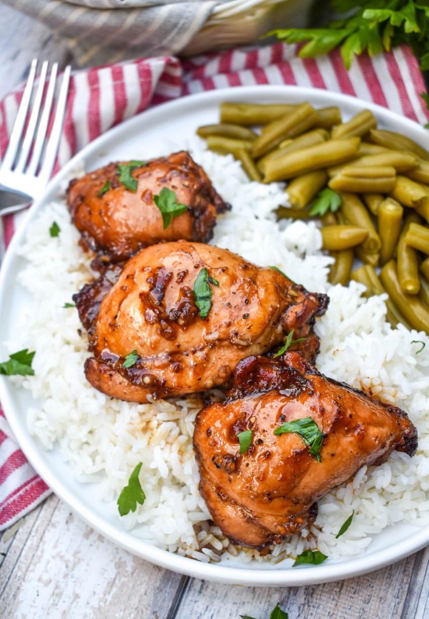 three balsamic chicken thighs over steamed white rice on a white plate