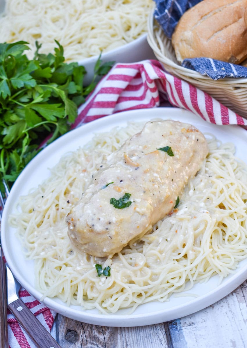 a slice of crockpot creamy angel chicken resting on a bed of angel hair pasta on a white plate