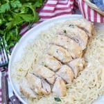 slices of creamy angel chicken over angel hair pasta on a white plate