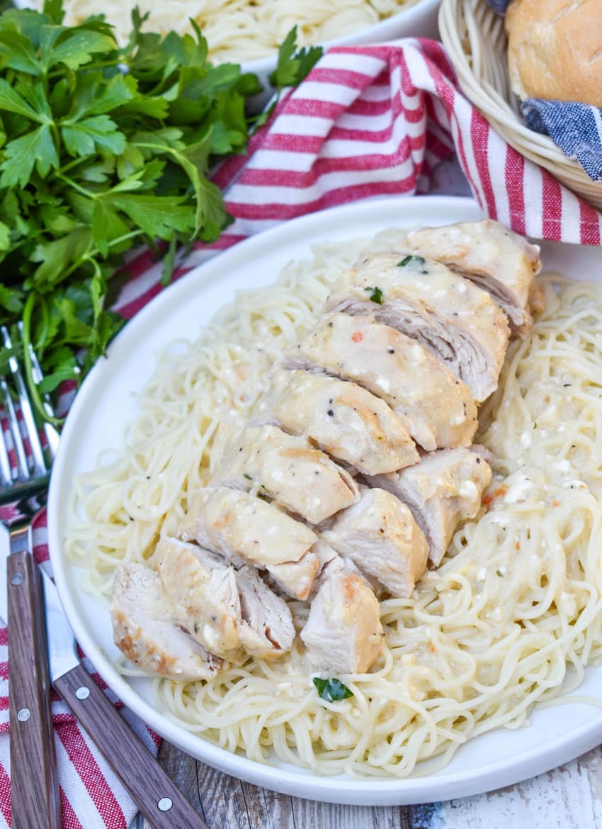 slices of creamy angel chicken over angel hair pasta on a white plate