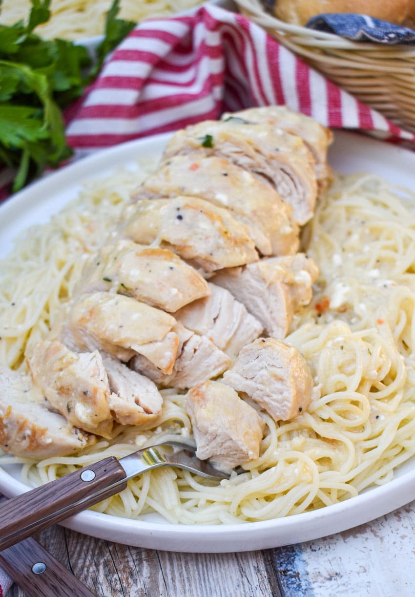 slices of creamy angel chicken over angel hair pasta on a white plate