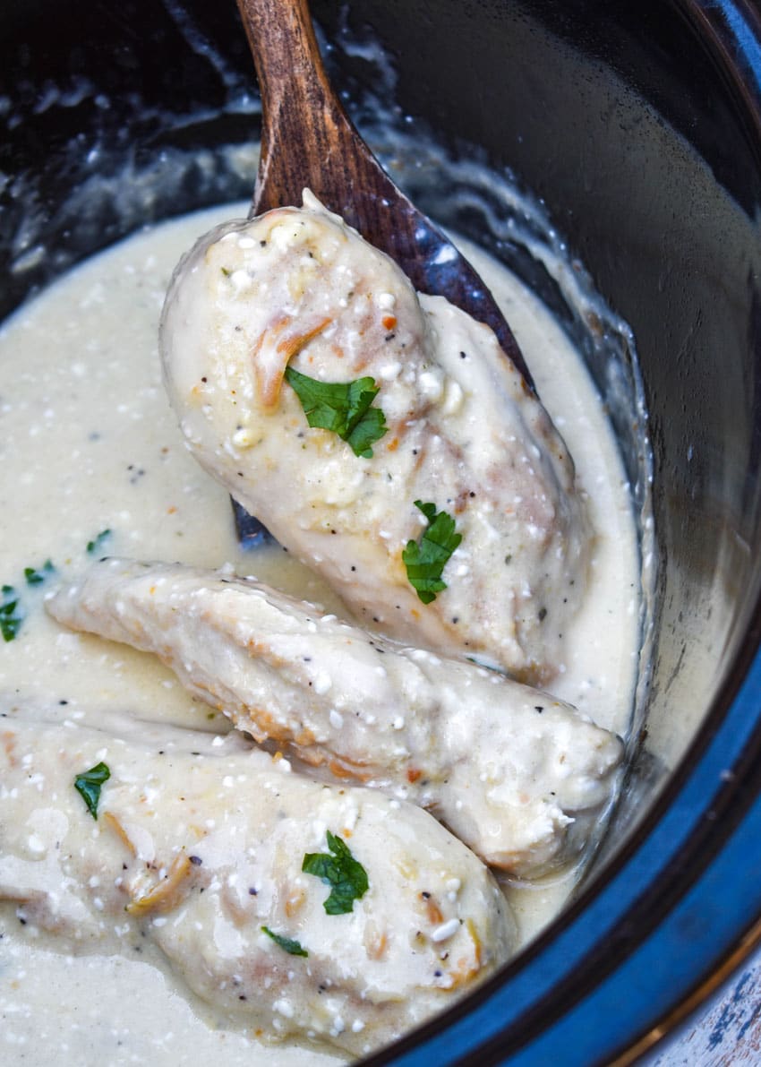 a wooden spatula slices of creamy angel chicken out of a black slow cooker