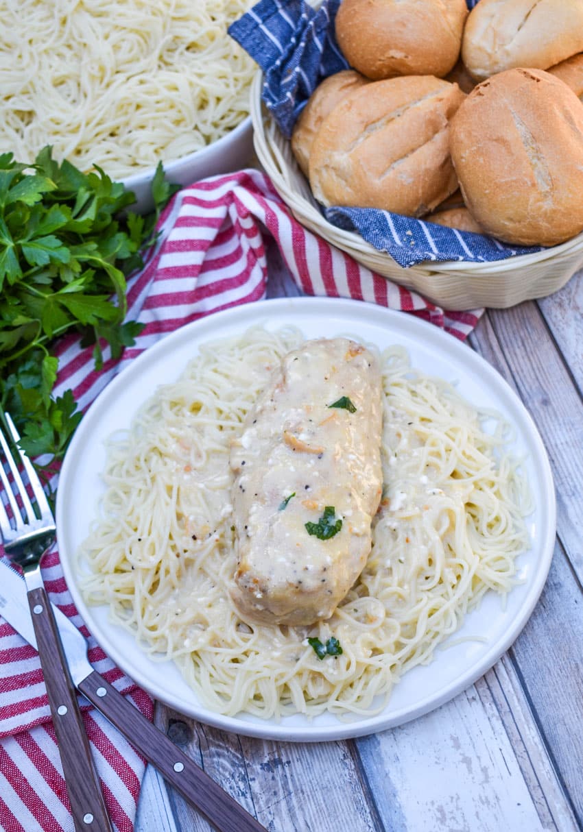 a slice of crockpot creamy angel chicken resting on a bed of angel hair pasta on a white plate