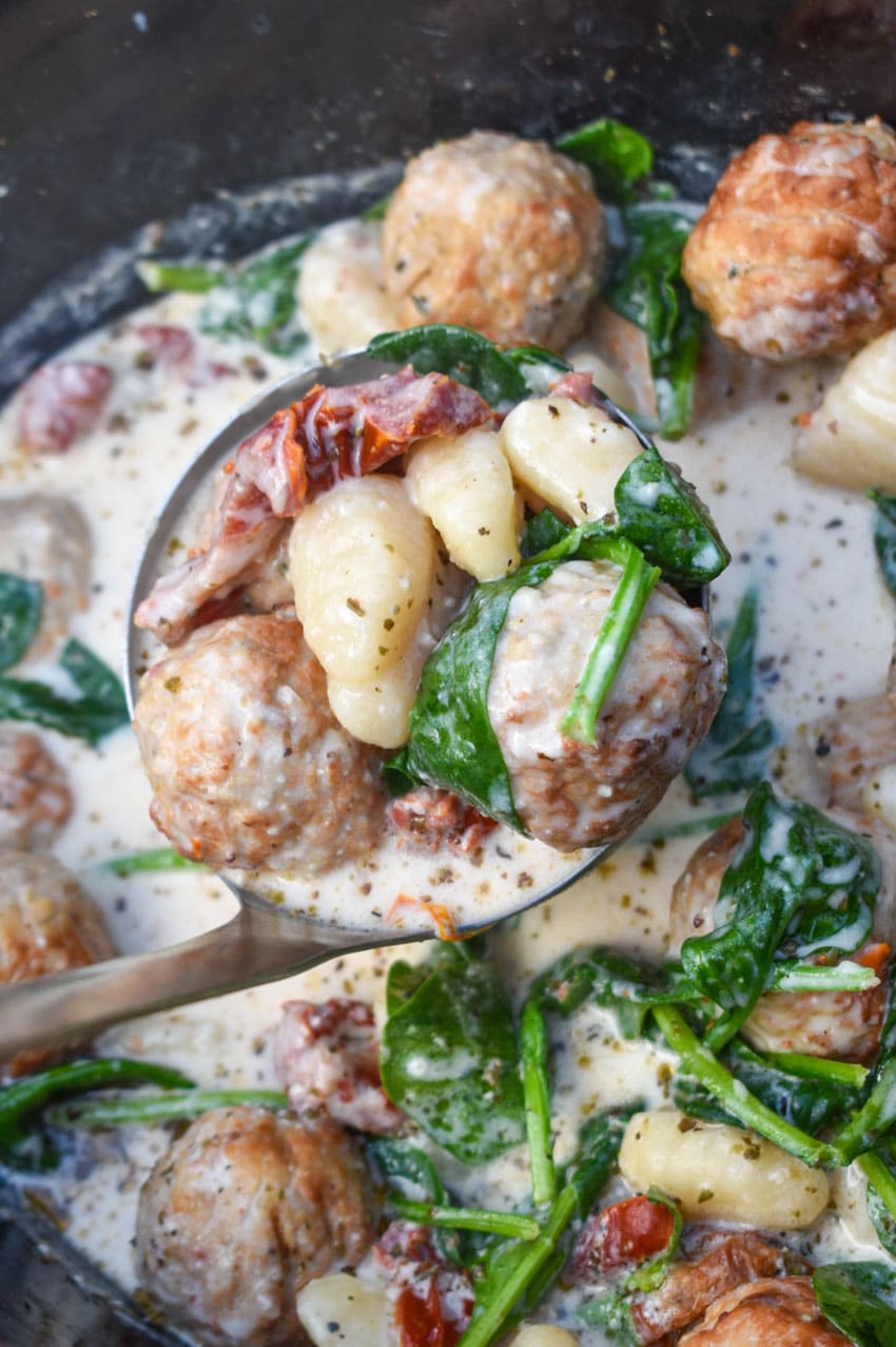 a silver ladle holding up a scoop of marry me meatballs with gnocchi