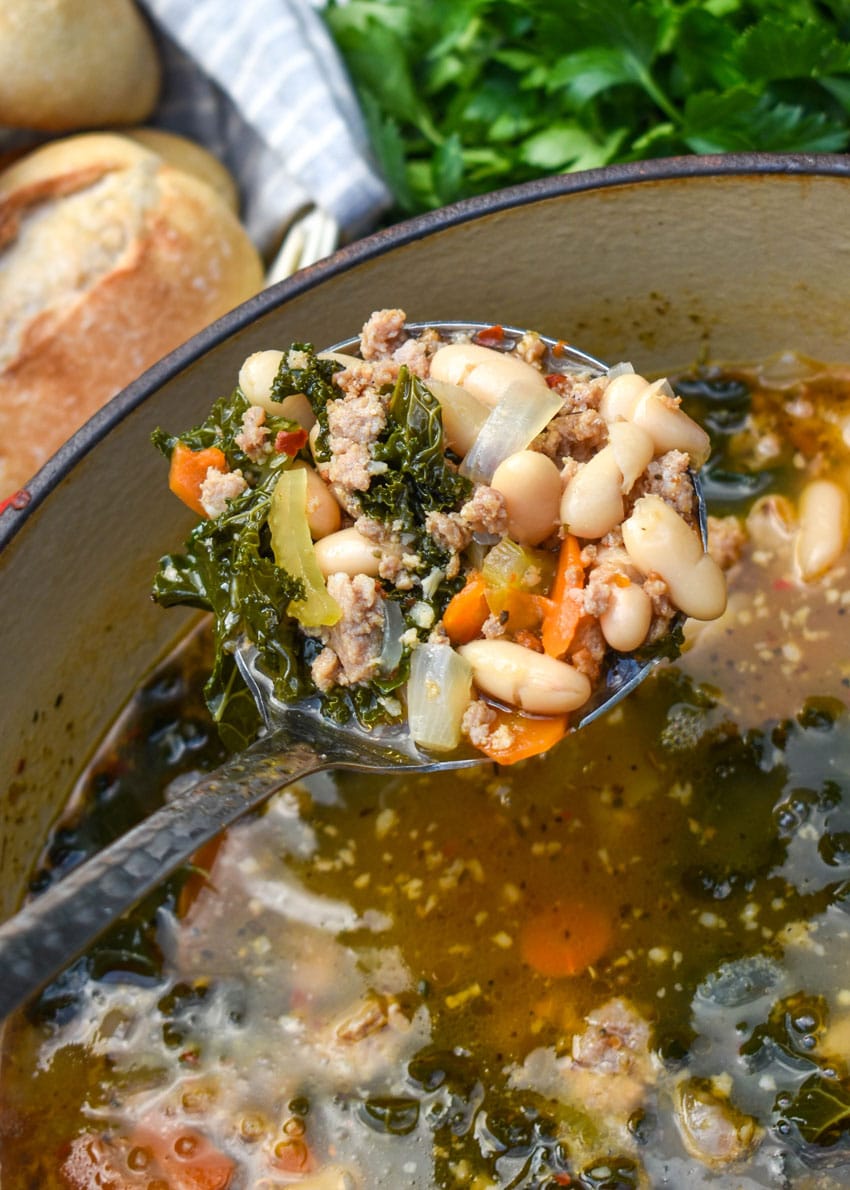 a silver ladle holding up a scoop of tuscan white bean soup with kale
