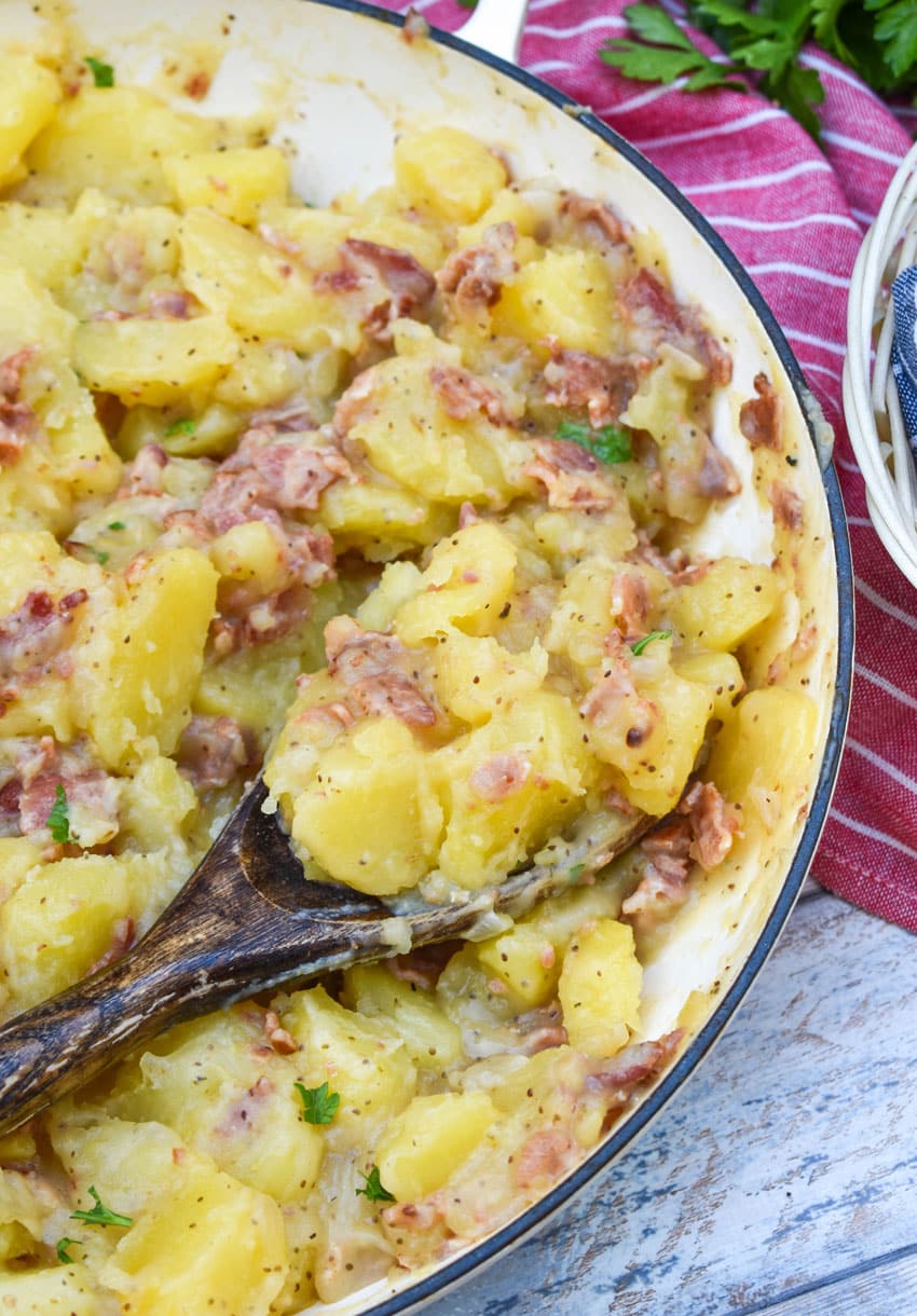 a wooden spoon scooping homemade german potato salad out of a large white skillet