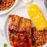 air fryer ribs next to baked beans and corn on the cob on a white plate