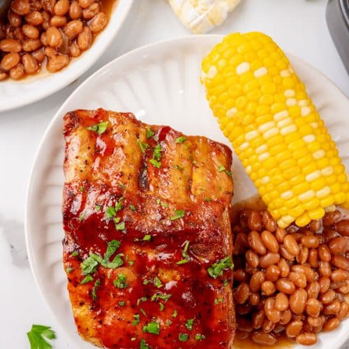 air fryer ribs next to baked beans and corn on the cob on a white plate