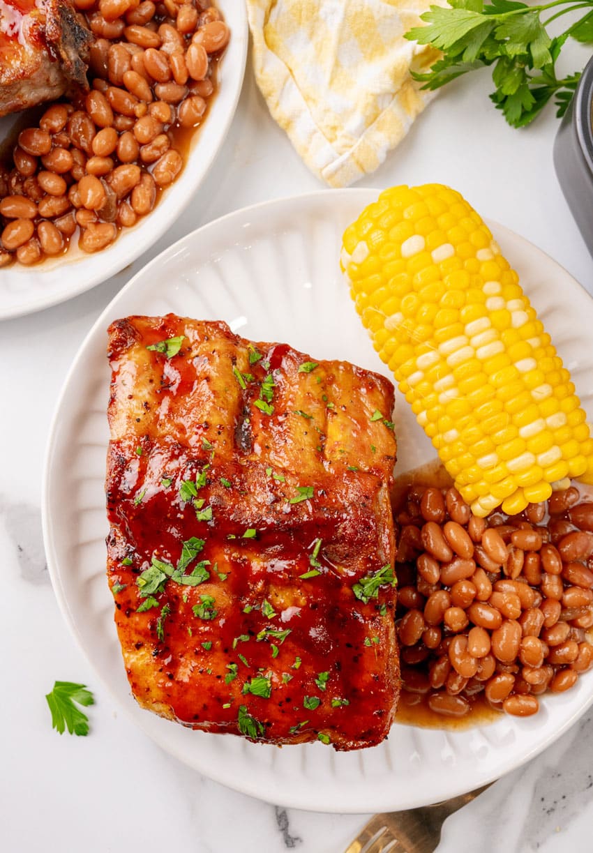 air fryer ribs next to baked beans and corn on the cob on a white plate