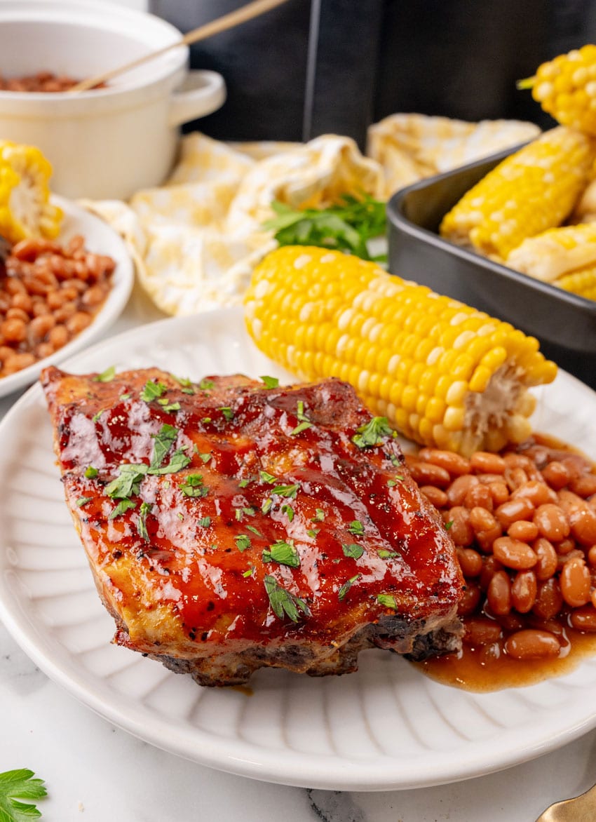 air fryer ribs next to baked beans and corn on the cob on a white plate