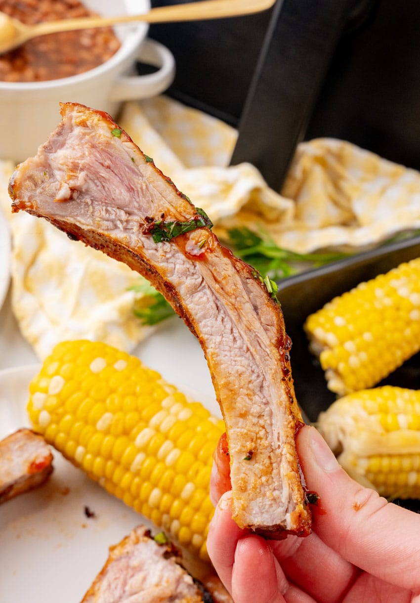 air fryer ribs next to baked beans and corn on the cob on a white plate