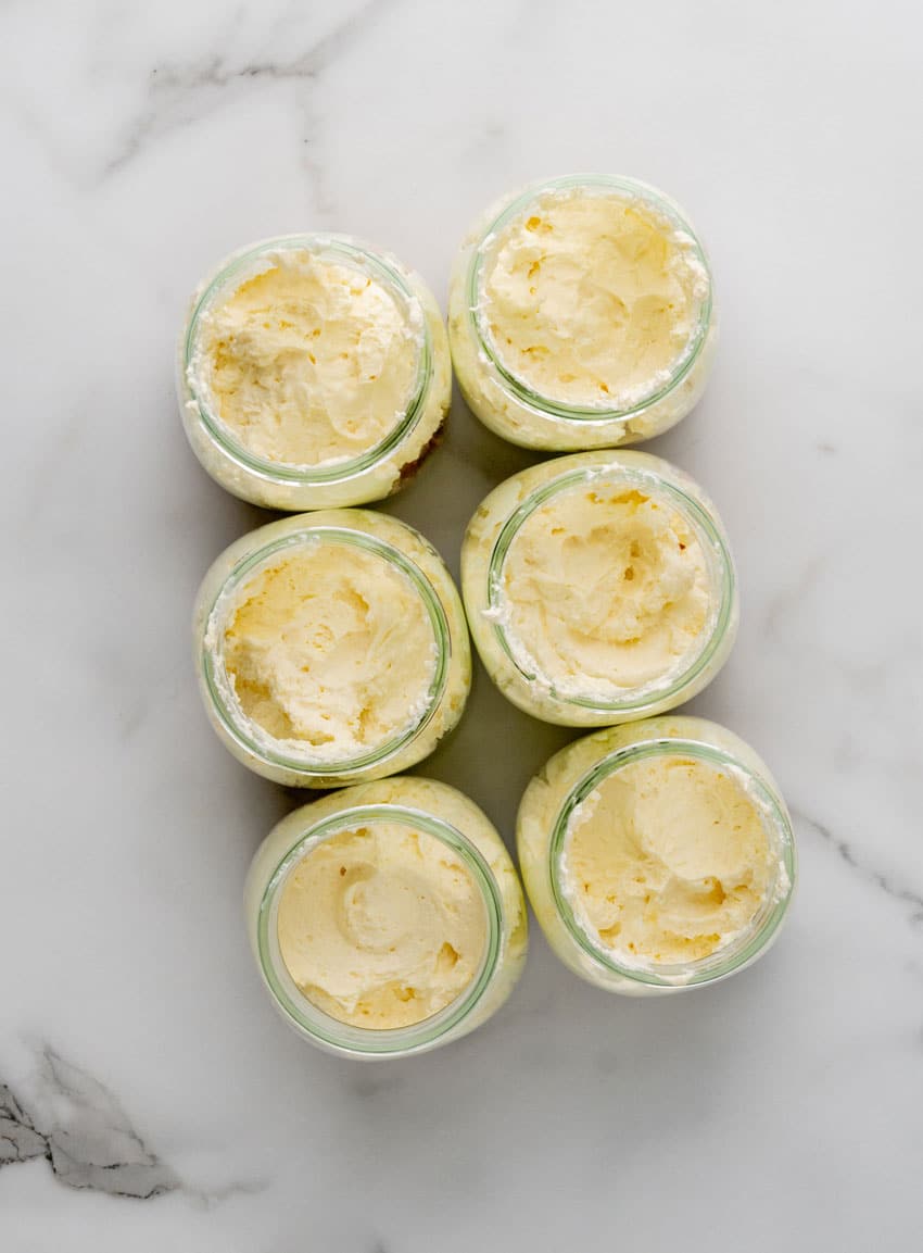 a layer of cheesecake filling in the bottom of six glass jars arranged in two rows