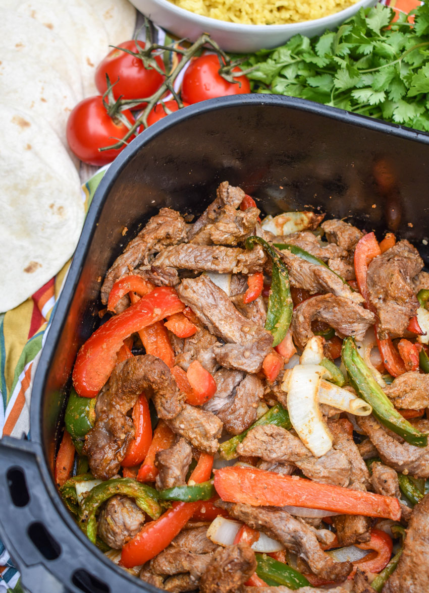 cooked seasoned steak strips and vegetables in the basket of an air fryer