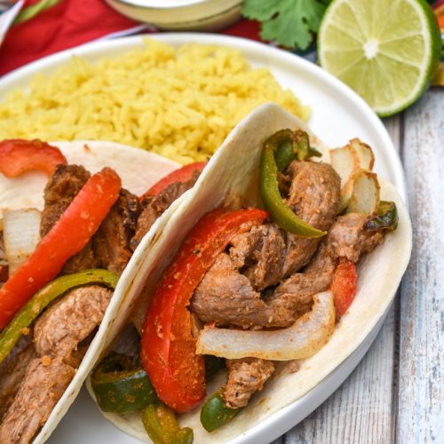 air fryer steak fajitas in flour tortillas on a white plate