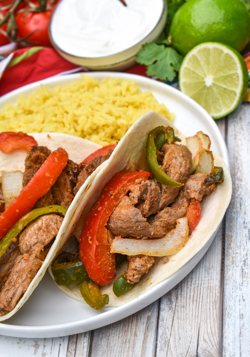air fryer steak fajitas in flour tortillas on a white plate