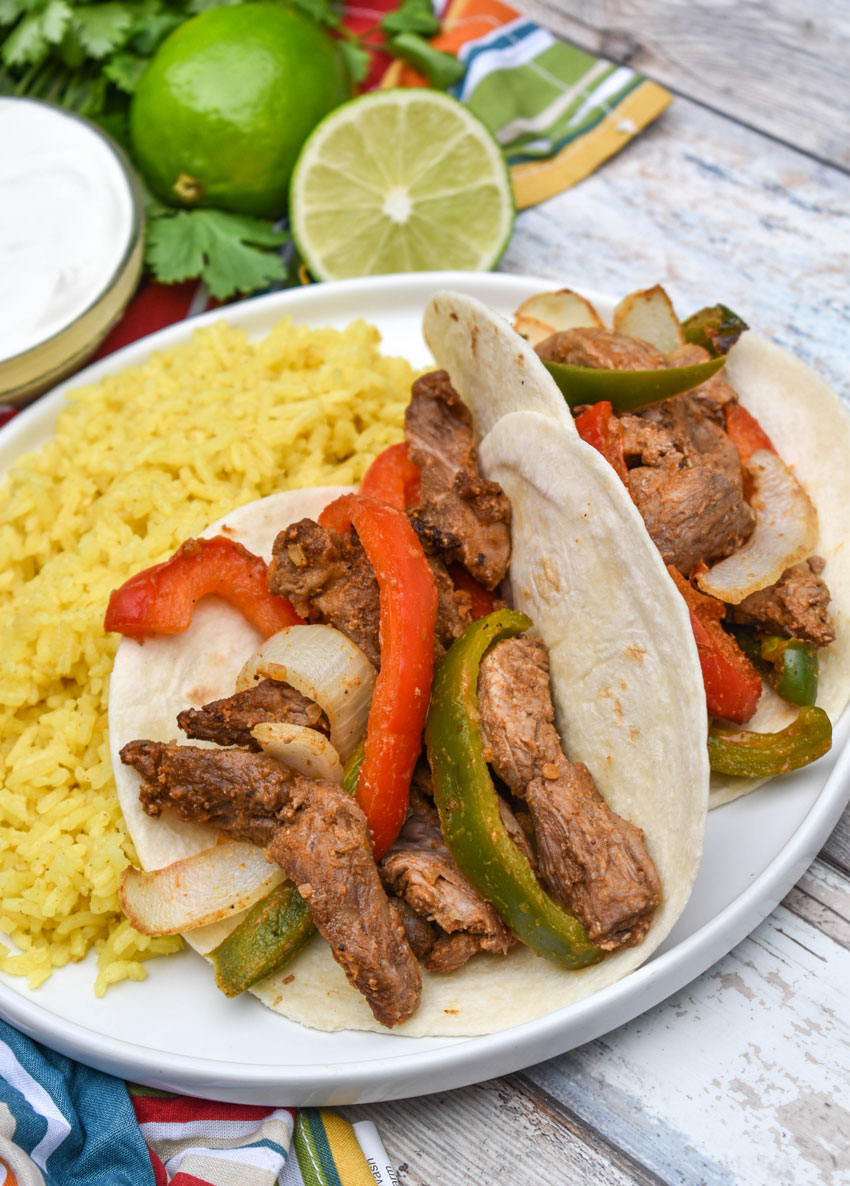 air fryer steak fajitas in flour tortillas on a white plate