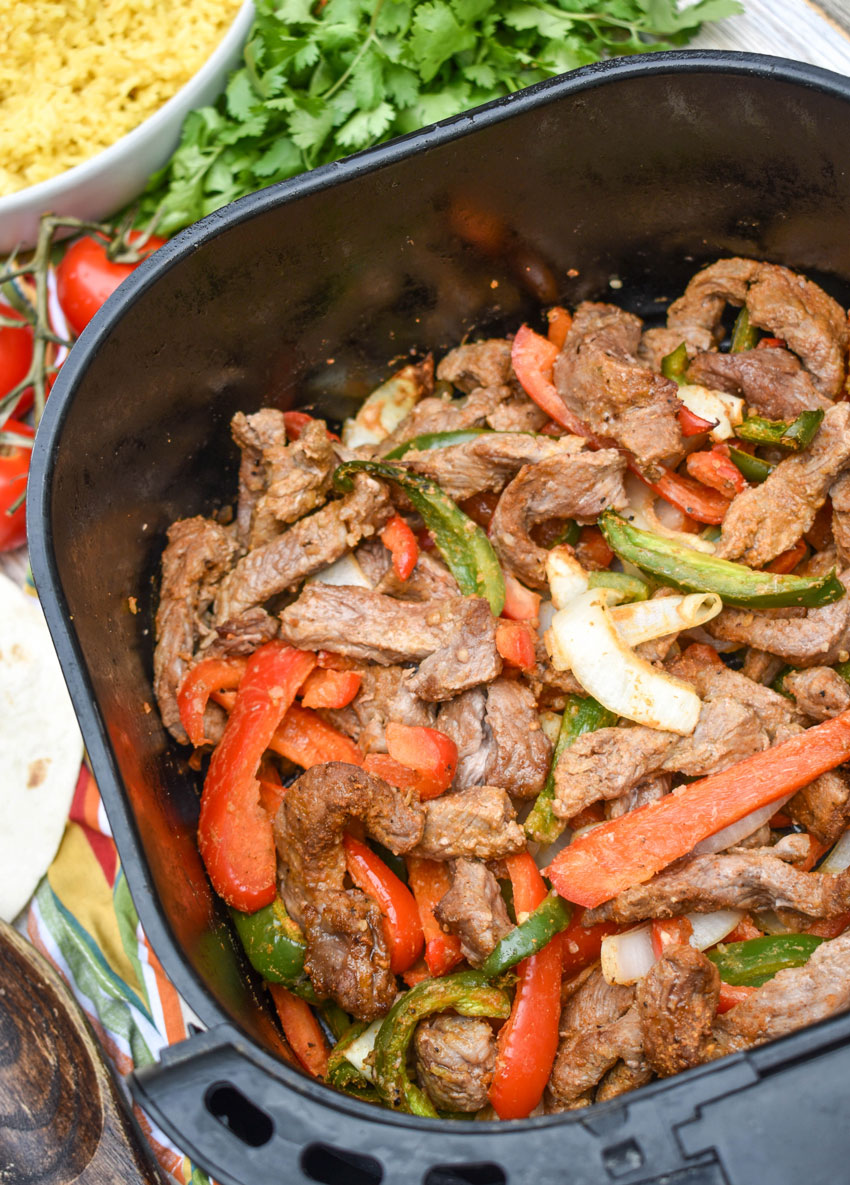 cooked seasoned steak strips and vegetables in the basket of an air fryer
