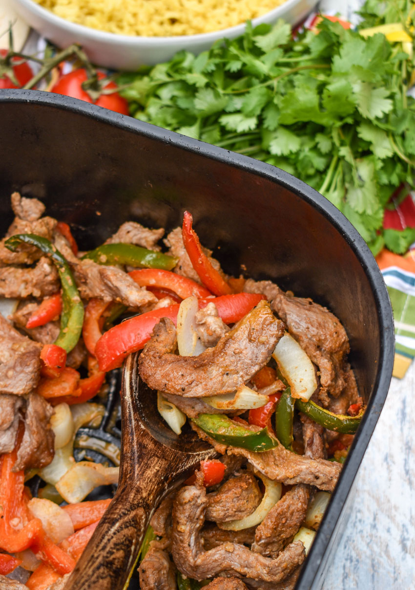 a wooden spoon scooping homemade steak fajita meat and vegetables out of the basket of an air fryer