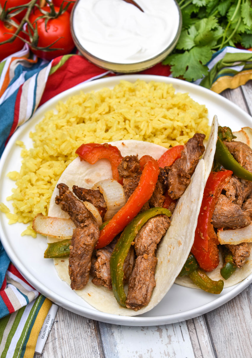 air fryer steak fajitas in flour tortillas on a white plate