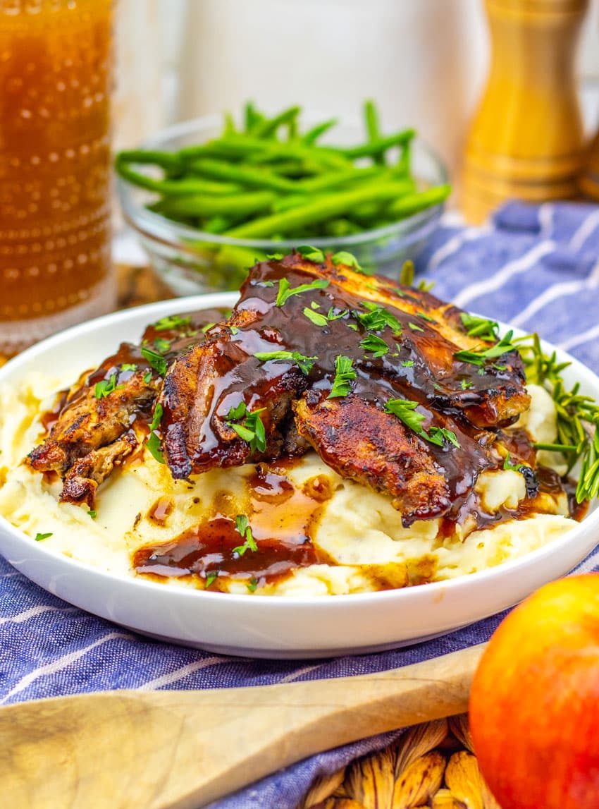 apple cider glazed pork chops over mashed potatoes in a shallow white bowl