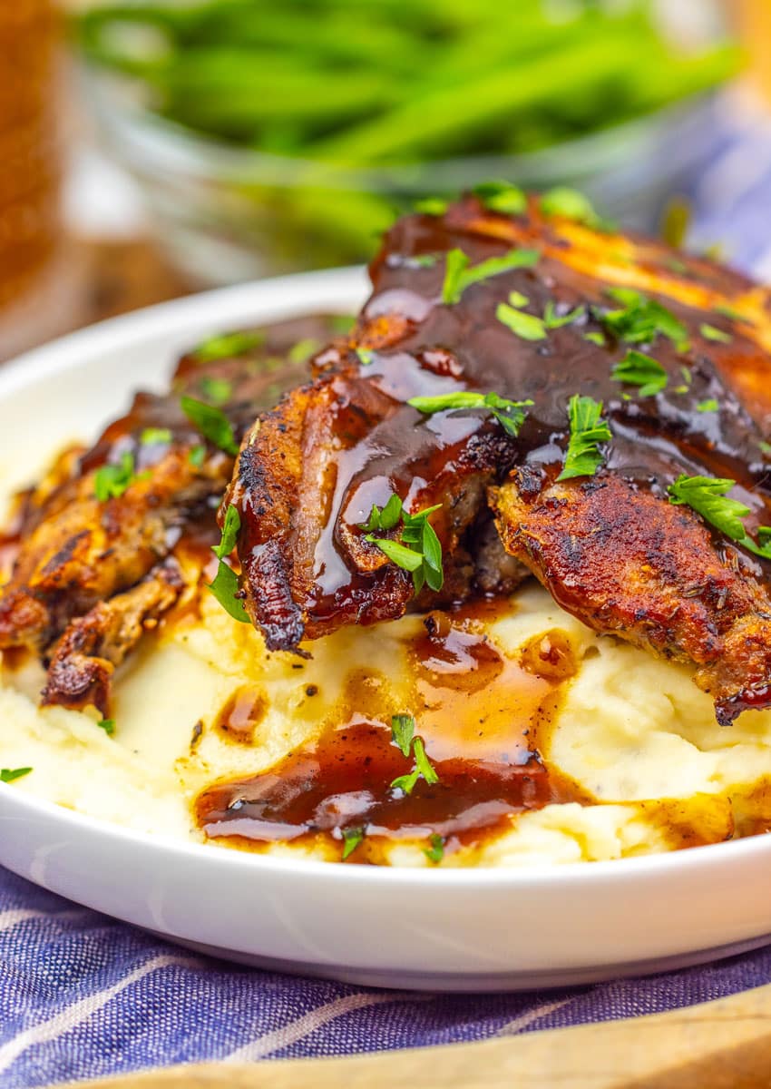 apple cider glazed pork chops over mashed potatoes in a shallow white bowl