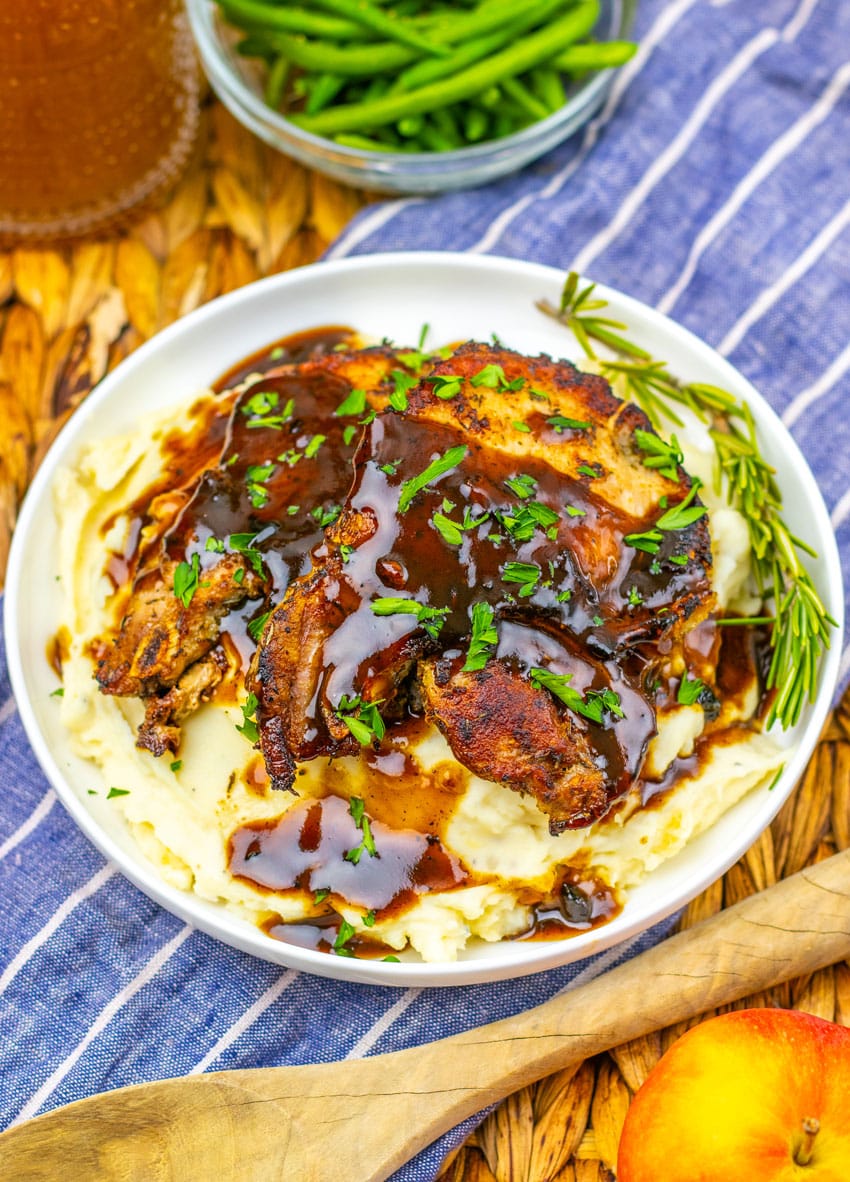 apple cider glazed pork chops over mashed potatoes in a shallow white bowl