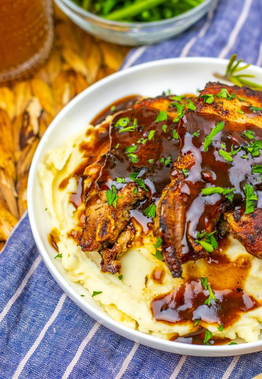 apple cider glazed pork chops over mashed potatoes in a shallow white bowl