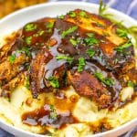 apple cider glazed pork chops over mashed potatoes in a shallow white bowl