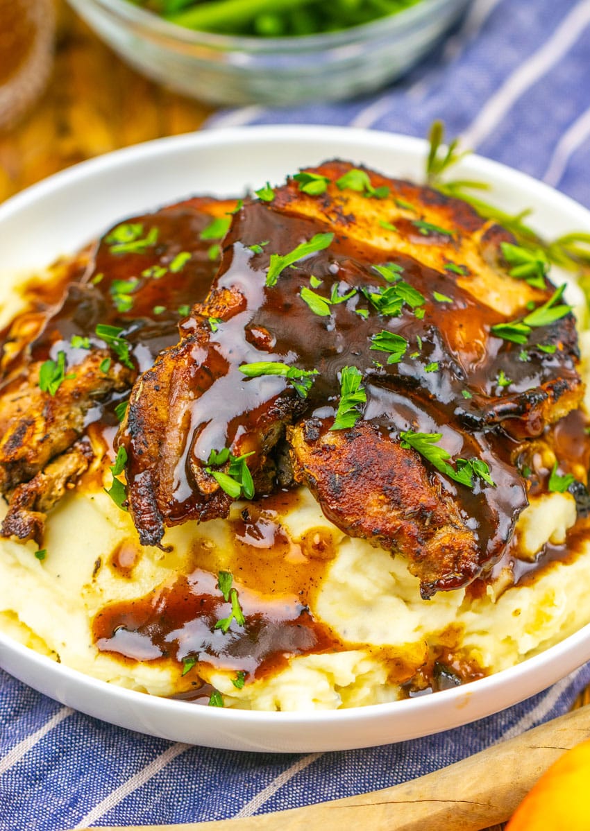 apple cider glazed pork chops over mashed potatoes in a shallow white bowl