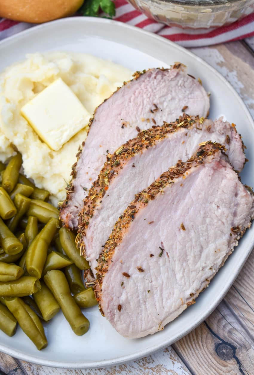 slices of Italian porchetta next to green beans and mashed potatoes on a white plate