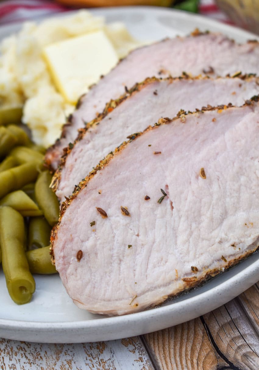 slices of Italian porchetta next to green beans and mashed potatoes on a white plate