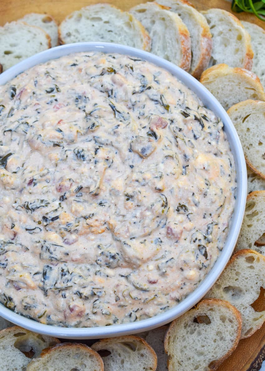 fiesta spinach dip in a shallow white bowl surrounded by slices of baguette bread