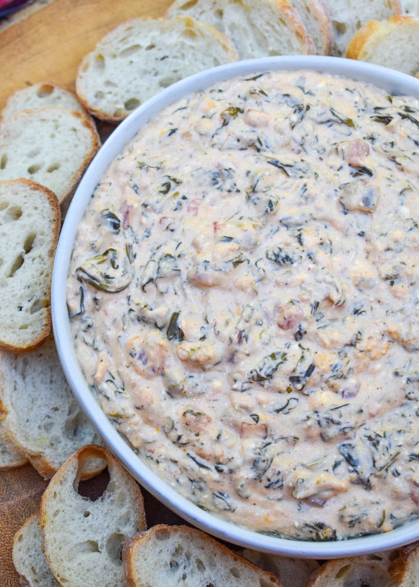 fiesta spinach dip in a shallow white bowl surrounded by slices of baguette bread