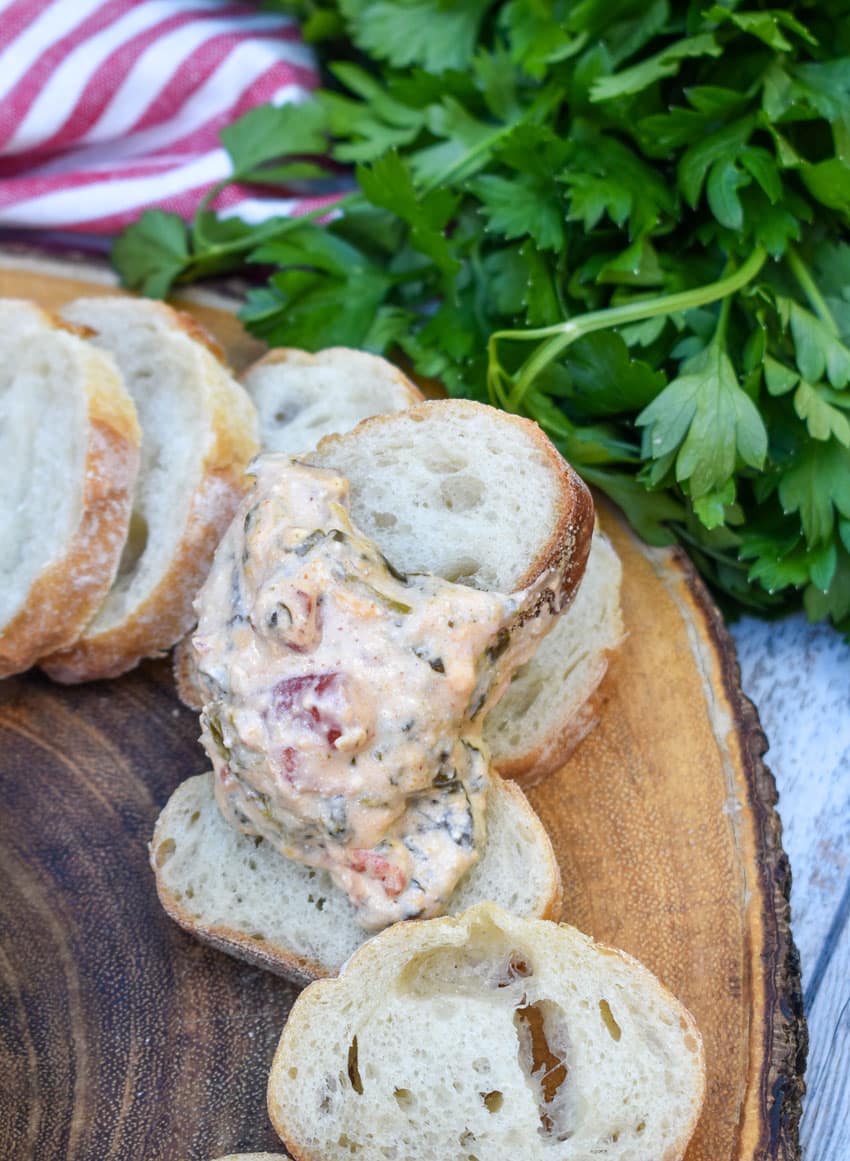 a slice of baguette bread topped with slow cooker spinach dip resting on a wooden cutting board