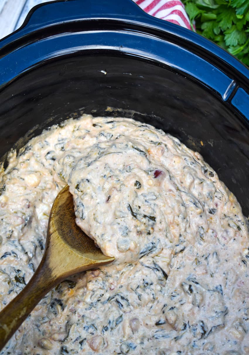 a wooden spoon scooping fiesta spinach dip out of the black bowl of a slow cooker