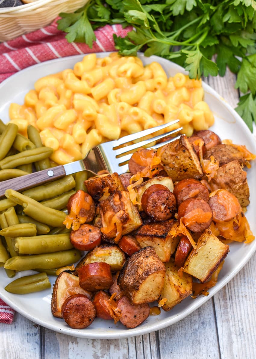 cheesy sheet pan hot dogs and potatoes on a white plate